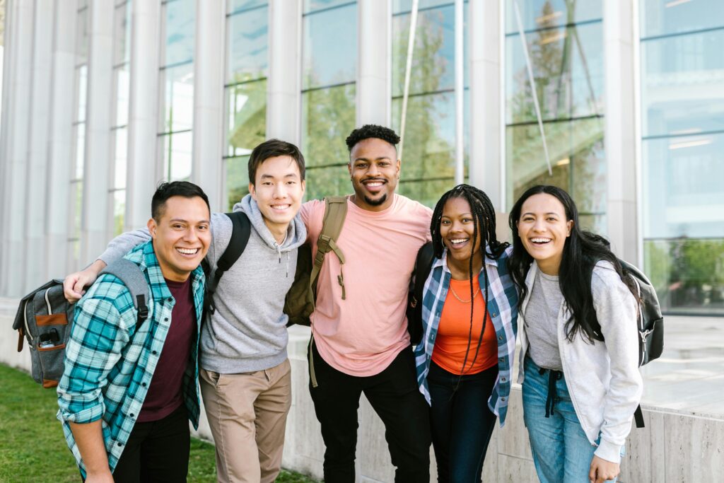 A diverse group of young adults smiling and standing together in front of a modern glass building.