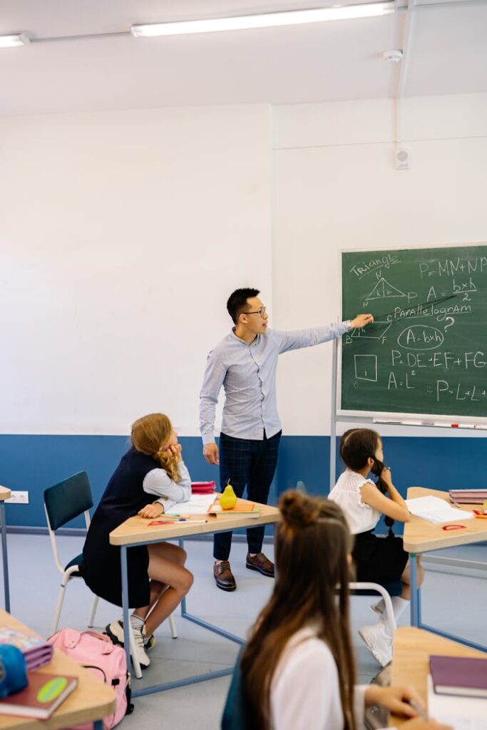 Teacher points to geometry equations on blackboard in a classroom setting.